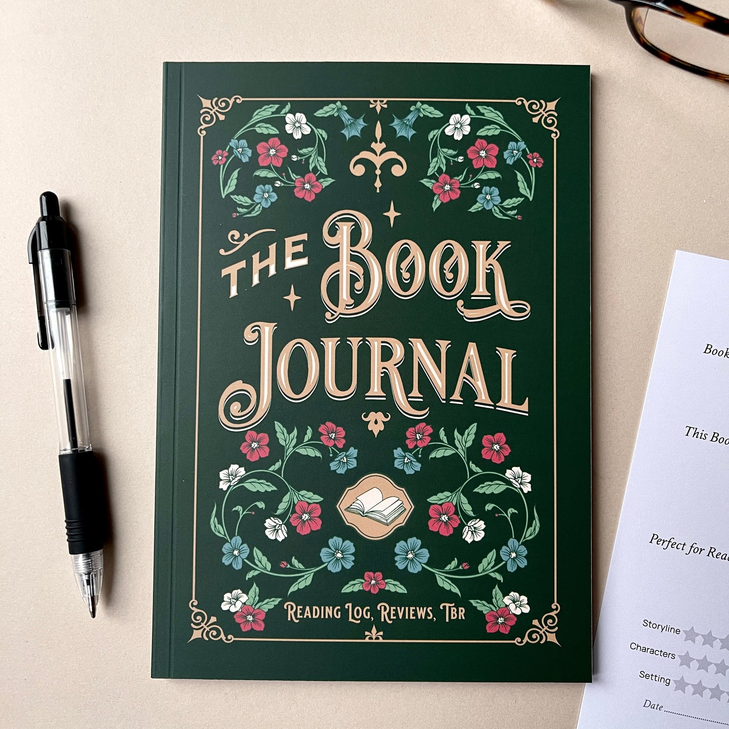 Book Journal with floral design on a beige surface with a pen and paper.
